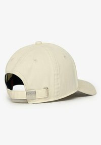Cream-colored baseball cap with a curved brim, adjustable strap at the back, and metallic logo accent. Made from durable fabric.