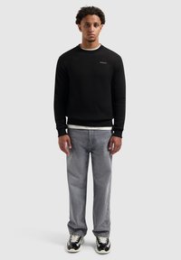 Zwart sweatshirt met een ronde hals en klein logo, gecombineerd met lichtgrijze jeans en zwart-witte sneakers. Soepele textuur, casual pasvorm.