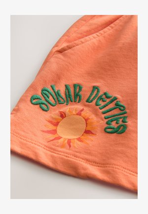 Il tessuto di cotone arancione presenta del testo ricamato in verde "Solar Deities" sopra una grafica del sole con raggi gialli e arancioni.