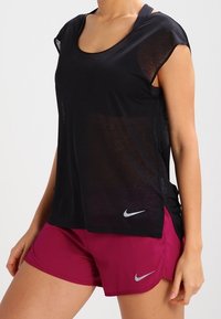 Czarna sportowa koszulka z krótkimi rękawami i okrągłym dekoltem, zestawiona z fuksjowymi szortami z srebrnymi logo Nike na obu.