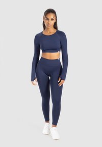 Marineblaues, kurz geschnittenes langärmeliges Oberteil und hoch taillierte Leggings aus dehnbarem Material. Kombiniert mit weißen Sportschuhen.