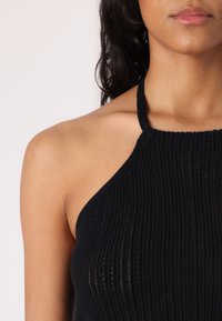 Μαύρο πλεκτό halter-top με ριμπ υφή και λεπτές τιράντες. Διαθέτει εφαρμοστό σχέδιο που αναδεικνύει ένα ανοιχτό ντεκολτέ.