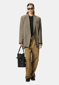 Blazer grigio oversize, t-shirt nera, pantaloni beige a gamba ampia con tasca cargo, borsa a tracolla nera, dettagli in seta bianca, occhiali da sole scuri.