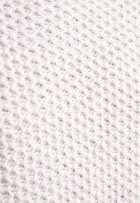 Tissu tricoté de couleur beige clair avec un motif tissé texturé. Apparence douce et légèrement duveteuse avec des fils de différentes épaisseurs.