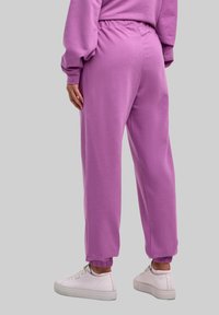 Fioletowe spodnie dresowe z elastycznym pasem i ściągaczami, o gładkiej teksturze. W zestawie z białymi trampkami.