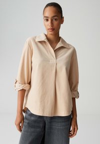 Light beige, collared blouse with a relaxed fit, 3/4 rolled sleeves, and a partial placket. Soft fabric texture; casual design.