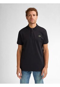 Černé polo tričko vyrobené z bavlny, s třemi knoflíky na léze, krátkými rukávy a zelenou logovou nášivkou na levé hrudi.