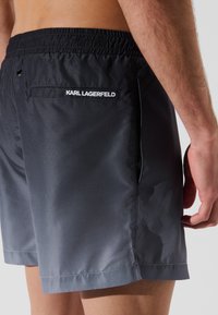 Tamsiai pilkos maudymosi šortai iš lygios medžiagos. Yra elastinga juostos dalis ir galinis kišenė su "KARL LAGERFELD" logotipu.
