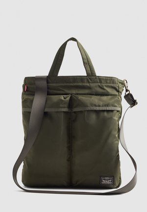 Olivengrønn polstret tote bag med to korte håndtak og en lang justerbar stropp. Har frontlomme og merke-logo applikasjon.