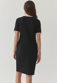 Czarna sukienka z krótkim rękawem o slim fit, z beżowym wykończeniem na rękawach i dekolcie, wykonana z miękkiego materiału, sięgająca do kolan.