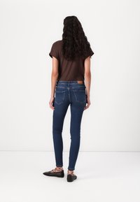 Skinny jeans in dark blue denim with pocket detailing, paired with a brown short-sleeve top. Black flat shoes complete the outfit.