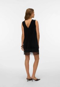 Svart sammetsklänning med V-formad ryggdesign och spetskant. Har en lös passform och är utan ärmar, når till mitten av låret.