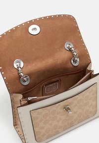 Beige laukku, jossa on kuviollinen nahkaulkopinta, mokkanahka sisäpinta, hopeiset yksityiskohdat, ketjuakselit ja vetoketjullinen tasku.