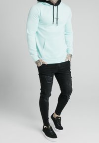 Světle modrá mikina s černými detaily a přední kapsou, spárovaná s černými roztrhanými skinny džíny a černými teniskami s bílou podrážkou.