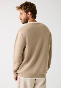Maglione beige lavorato a maglia con colletto rotondo, orlo e polsini a coste, texture morbida e vestibilità rilassata, visto da dietro.