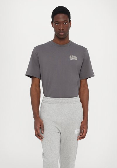 Grey cotton t-shirt with short sleeves and a crew neckline, featuring a small white logo on the left chest. Worn with light grey sweatpants.