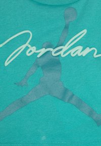 T-shirt en coton turquoise présentant une grande silhouette translucide de Jumpman et le logo "Jordan" en lettres blanches légèrement surélevées.