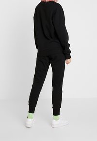 Sudadera negra y joggers a juego hechos de un tejido suave, con puños y cinturilla elásticos, combinados con zapatillas blancas y calcetines verdes.