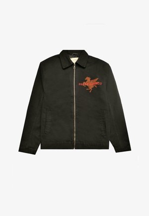 Jachetă neagră cu fermoar în față, guler ascuțit și un design brodat cu un cal portocalie, însoțit de textul "PAS DE MONACO" pe zona din stânga pieptului.