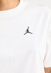 Hvit bomull T-skjorte med en liten svart brodert Air Jordan-logo på venstre brystområde. Korte ermer, enkelt design.