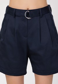 Shorts taille haute bleu marine avec une ceinture dotée d'une boucle en argent, devant plissé et ourlets roulés. Fabriqués en mélange de coton texturé.