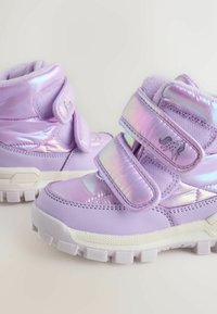 Lila Kinderstiefel mit glänzender Lackoberfläche, zwei Klettverschlüssen, strukturierten Stoffakzenten und einer robusten weißen Sohle.