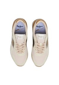 Beige sneakers with a textured finish, featuring a dark vertical stripe, round toe, and beige laces. Accented with gold branding.