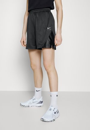 Czarne sportowe spodenki z siateczkowej tkaniny oraz bocznymi rozcięciami, z białym logo Nike. W komplecie z białymi butami sportowymi i skarpetkami do kostki.
