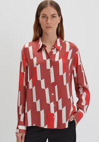 Rood en wit gestreepte overhemd met lange mouwen, kraag, knoopsluiting aan de voorkant en een gladde, satijnachtige textuur. Heeft geometrische vormen.