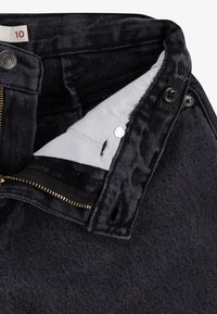 Jean en denim noir avec une fermeture éclair, un bouton de fermeture et une doublure intérieure douce. Le tissu présente une texture côtelée subtile.