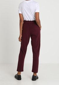 Bordeauxbroek met een relaxte fit, voorzien van een hoge taille en een elastische tailleband, gecombineerd met een wit T-shirt met korte mouwen en zwarte schoenen.