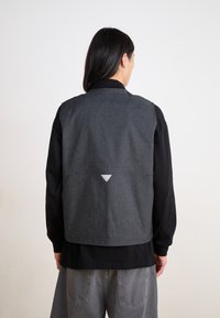 Gray vest with a textured finish, featuring a triangular reflective accent at the back, layered over a black long-sleeve shirt.