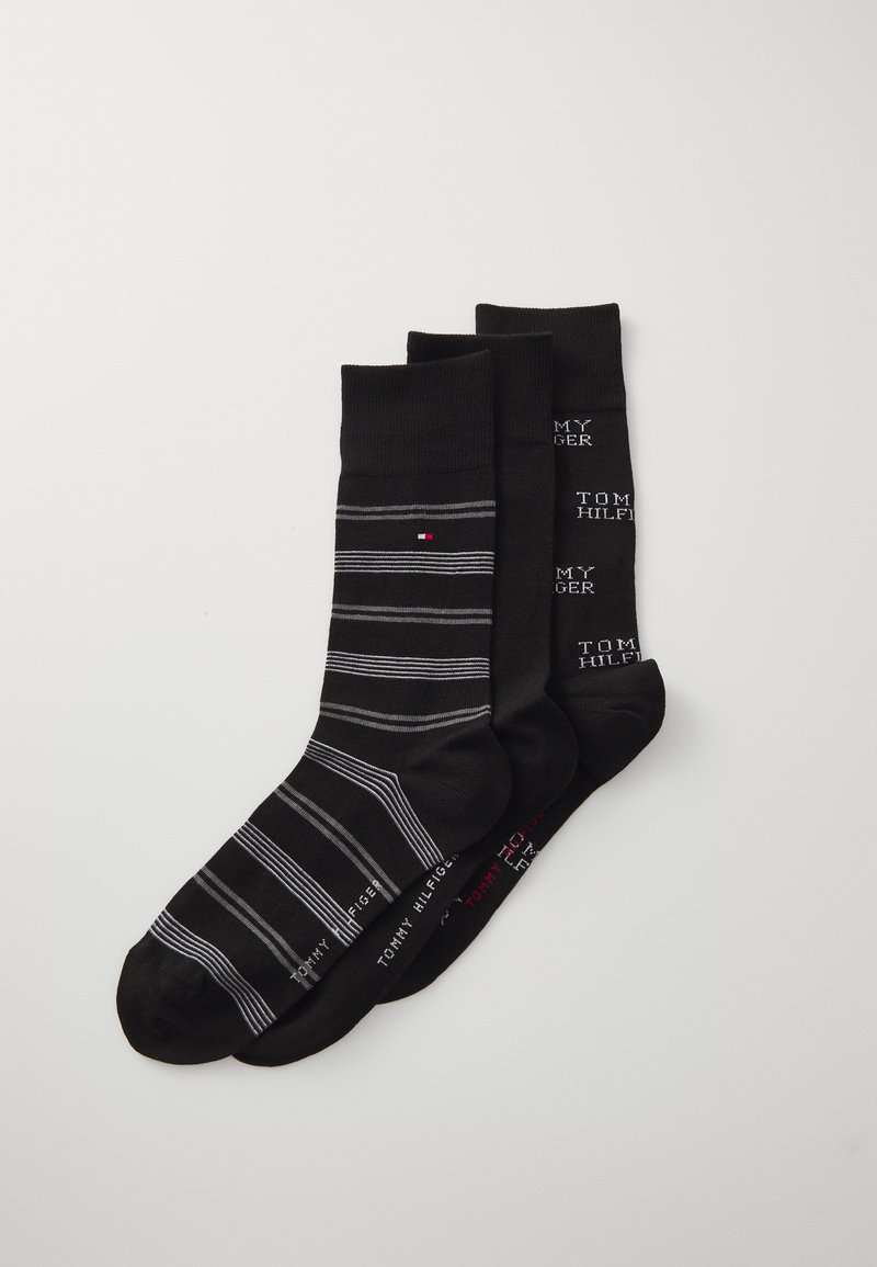 Tres pares de calcetines: uno negro con rayas grises, uno negro sólido y uno con texto repetido en blanco y negro, con acentos del logo.