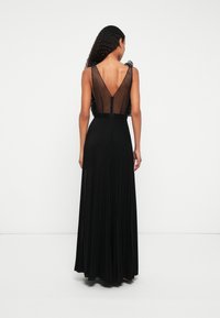 Vestido maxi preto plissado com costas transparentes, decote em V e detalhes de ombros com babados. Tecido texturizado com forro suave e fecho com zíper.