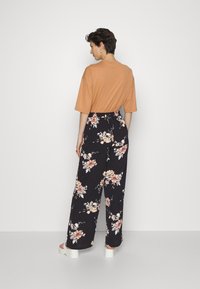 Top laranja de mangas curtas combinado com calças largas pretas com flores em tons de rosa e creme, cintura elástica e sandálias brancas planas.