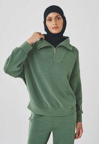 Green sweatshirt with a high collar and quarter-zip, made of soft material. Features relaxed fit and ribbed cuffs and hem.