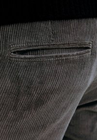 Poche arrière avec ouverture fendue sur un pantalon en velours côtelé gris foncé, gros plan montrant la texture du tissu et les détails de la couture.