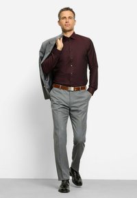 Bordeauxfarbendes Hemd mit Knöpfen, graue gemusterte Hose, brauer Gürtel und schwarze Schuhe. Grauer Blazer, über die Schulter gelegt, bietet Kontrast.