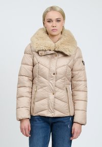 Beige kviltet puffjakke med en faux fur krave, guld lynlåsdetaljer og en tætsiddende silhuet. Har skrå syninger og trykknaplukninger.