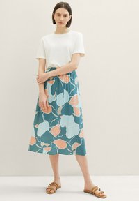 Haut blanc léger à manches courtes associé à une jupe midi florale teal avec des motifs pêche et bleu, taille élastique et sandales plates.