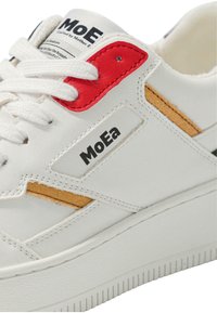 Baltas ādas sporta kurpes ar teksturētu virsmu, sarkaniem un brūniem akcentiem, kā arī melnu zīmolu. Iezīmējas ar izturīgu balto zoli un auduma šņorēm.