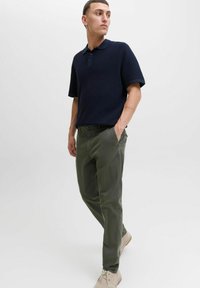 Granatowa, teksturowana koszulka polo z krótkim rękawem, zestawiona z oliwkowymi chinosami. Model nosi beżowe buty i ma ręce w kieszeniach.