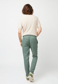 Beige textured knit shirt with short sleeves, paired with green tapered pants. Footwear features light soles and green accents.