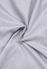 Textielstof met een lichtgrijze achtergrond en een subtiel geruit patroon in donkergrijs en blauw. Zachte textuur met een vloeiende kwaliteit.