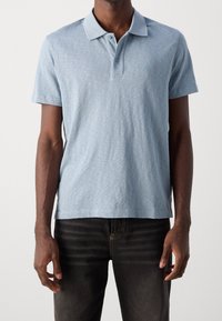 Ljusblå pikétröja av mjukt tyg, med en treknappslinning, korta ärmar och subtil struktur. Bärs med mörka jeans.