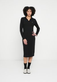 Schwarzes langärmliges Kleid mit Kragen und schlanker Passform, das ein dezentes Logodetail aufweist. Glatter Stoff, knielanges Design.