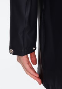 Black waterproof jacket sleeve, smooth texture, features a snap closure and metallic accent at the cuff, with a fitted design.
