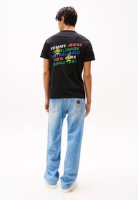 Sort T-shirt med multikolor tekst på bagsiden, parret med lyseblå jeans. T-shirten har rund halsudskæring og korte ærmer.