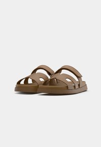 Sandales en caoutchouc marron avec plusieurs brides ouvertes, une semelle plate et des rainures texturées. Dispose de fixations réglables en crochet et boucle pour un ajustement parfait.