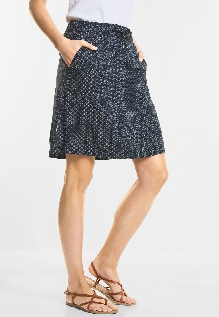 Jupe bleu foncé avec une texture à motifs, taille à cordon de serrage et poches latérales, assortie à des sandales marron à brides.